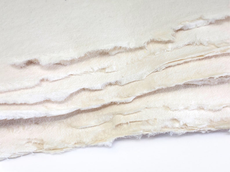 K&ouml;nnte beinhalten: Ein Stapel handgesch&ouml;pften Papiers mit einer rauen, strukturierten Oberfl&auml;che. Das Papier ist cremefarben und hat eine leicht unregelm&auml;&szlig;ige Form.
