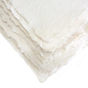 K&ouml;nnte beinhalten: Ein Stapel wei&szlig;er handgemachter Papiere mit einer rauen, strukturierten Oberfl&auml;che. Das Papier ist leicht uneben und hat ein nat&uuml;rliches, organisches Aussehen.
