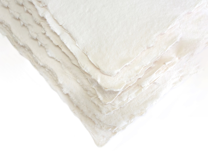 K&ouml;nnte beinhalten: Ein Stapel wei&szlig;er handgemachter Papiere mit einer rauen, strukturierten Oberfl&auml;che. Das Papier ist leicht uneben und hat ein nat&uuml;rliches, organisches Aussehen.