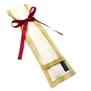 May include: A beige canvas pencil case with a gold trim and a red ribbon tied around it. The case has a black label that says "ARTWAY".
