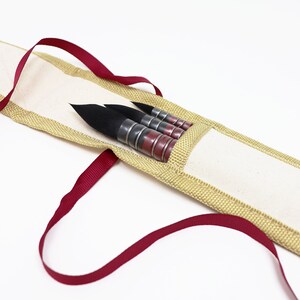 May include: A set of four black calligraphy brushes with red and silver handles are stored in a beige canvas case with a red ribbon.