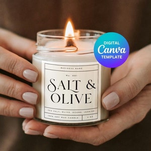 May include: A person is holding a lit candle in a clear glass jar with a white label that says "Salt & Olive" in black text. The label also includes the text "Sea Salt, Olive, Cedar, Jasmine" and "Soy Wax Candle". A blue circle with the text "Digital Canva Template" is in the upper right corner of the image.