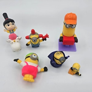 May include: A collection of six plastic character figurines including a girl on a white unicorn, a yellow minion with a red megaphone, a tall yellow minion in an orange hard hat, a minion in pink overalls, a minion in a blue cape, and a small minion.