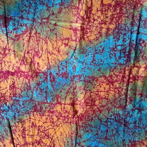 Könnte beinhalten: Nahaufnahme eines Stoffes mit Batik-Design. Der Stoff weist eine Mischung aus Farben auf, darunter Orange, Türkis und Burgunder. Das Design hat ein netzartiges Muster im gesamten Stoff.