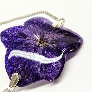 May include: A purple flower pressed inside a clear resin pendant with a silver chain.