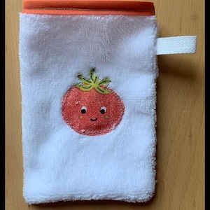 Peut inclure: Un gant de toilette blanc avec une bordure orange et une boucle blanche. Il présente une tomate rouge brodée avec un visage souriant. La tomate a des feuilles vertes et un contour rouge. Le gant est en tissu éponge.