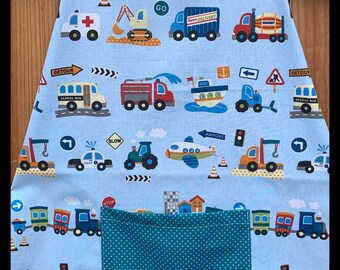 May include: A blue children's apron with a teal polka dot trim and a large pocket. The apron is covered in a print of various vehicles, including cars, trucks, buses, airplanes, and construction equipment. The print also includes traffic signs, such as "Go", "Slow", "Detour", and "Airport".