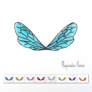 Könnte beinhalten: Ein Paar blaue Feenflügel mit Glitzer, die in Schwarz umrandet sind. Die Flügel werden vor einem weißen Hintergrund gezeigt. Der Text "Magicrealtion Passion" ist unter den Flügeln sichtbar.