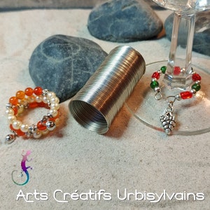 May include: Three different wine glass charms. One charm is a silver coil, one is a beaded charm with red and green beads, and the last is a silver charm with a grape design.