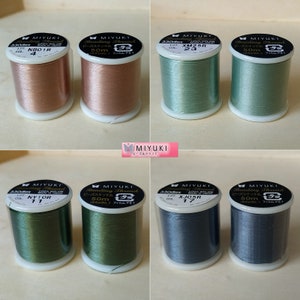 May include: Eight spools of Miyuki beading thread in a variety of colours, including pink, green, blue, and grey. Each spool is labelled with the brand name, thread type, and size. The spools are arranged in two rows of four.
