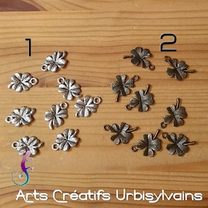 Op de afbeelding: Twee sets metalen klavertjevier bedels, één set in zilver en één set in brons. De bedels hebben een lus aan de bovenkant om te bevestigen aan sieraden of andere knutselwerkjes.