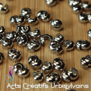 May include: A close-up of a group of silver metal crimp beads. The beads are small and round, with a hole in the centre. They are arranged in a random pattern on a wooden surface.
