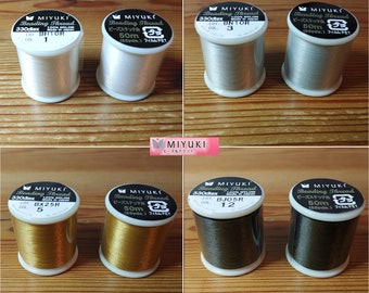 Può includere: Sei bobine di filo per perline Miyuki in vari colori, tra cui bianco, argento, oro e nero. Ogni bobina è etichettata con il nome del marchio, il tipo di filo e il numero di colore. Le bobine sono disposte in due file di tre.