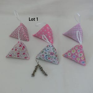 Peut inclure: Six sachets triangulaires en tissu avec des boucles de ruban blanc. Les sachets présentent divers motifs, dont des pois roses, des imprimés floraux et du vichy. Un petit bouquet de lavande séchée est également présent. Le texte "Lot 1" est visible.