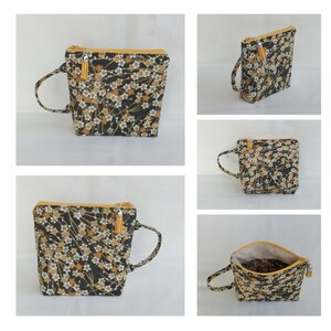 May include: A black and gold zippered pouch with a floral pattern and a small tassel. The pouch has a handle and can be used as a small bag.