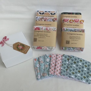 Può includere: Sono esposti diversi set di panni per il viso riutilizzabili con motivi floreali e geometrici. I panni sono confezionati in set da sette e si trovano accanto a una scatola regalo bianca con un'etichetta e un nastro festivi.