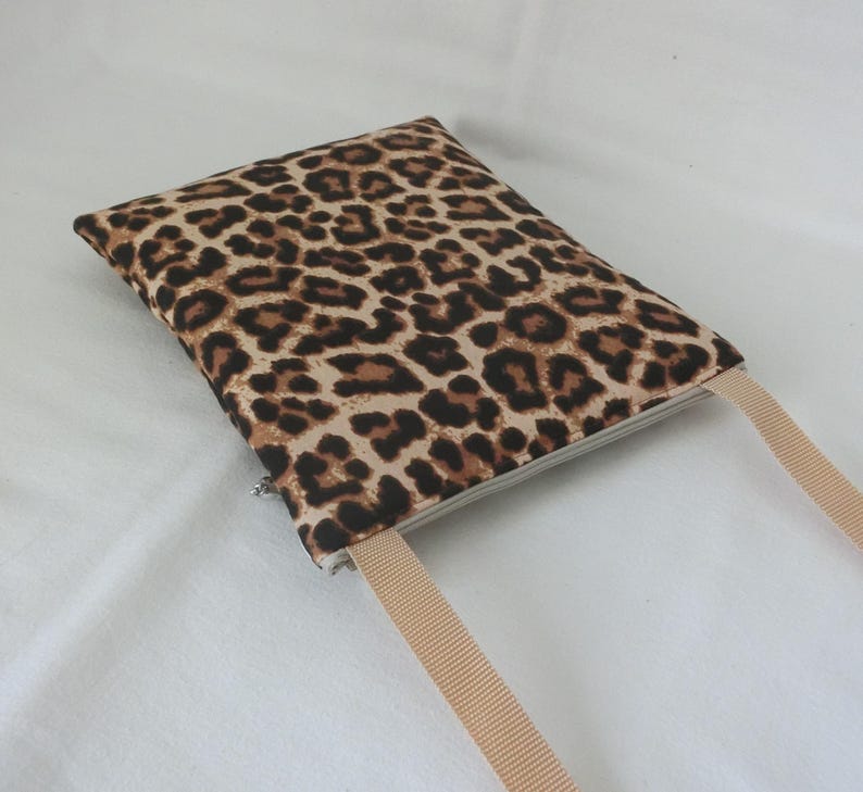May include: A rectangular, leopard print pouch with a beige strap. The pouch features a zipper closure and a repeating pattern of brown spots on a tan background. The strap is a solid beige color.