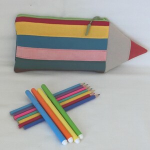 Peut inclure: Une trousse en forme de crayon avec un motif rayé coloré, avec une pointe rouge et un corps beige. Plusieurs crayons de couleur et stylos sont dispersés en dessous, dont des stylos bleus, verts, orange et jaunes, et une variété de crayons de couleur.