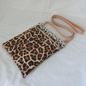 May include: A rectangular crossbody bag with a leopard print pattern in shades of brown and black. The bag has a beige strap and a zipper closure. The bag is made of fabric.