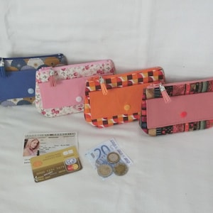 Może przedstawiać: Cztery ręcznie robione portfele z tkaniny w różnych wzorach i kolorach. Portfele mają prostokątny kształt z zamkiem błyskawicznym u góry i zapięciem na klapę. Jeden portfel jest niebieski we wzór kwiatowy, drugi różowy we wzór kwiatowy, a pozostałe dwa są pomarańczowe i różowe.