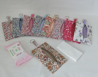 May include: A collection of floral fabric tissue holders in various colors, each with a key ring attachment. A package of wet wipes and a stack of white tissues are also present. The tissue holders feature a slit opening for easy access.