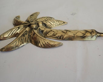 Puede incluir: Un gancho de metal dorado con forma de palmera. El gancho está hecho de metal y tiene un diseño detallado. Es una pieza decorativa y funcional.