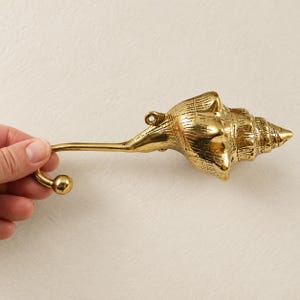 Hand holding a brass shell spiral hook, showing full length and curved hook end
