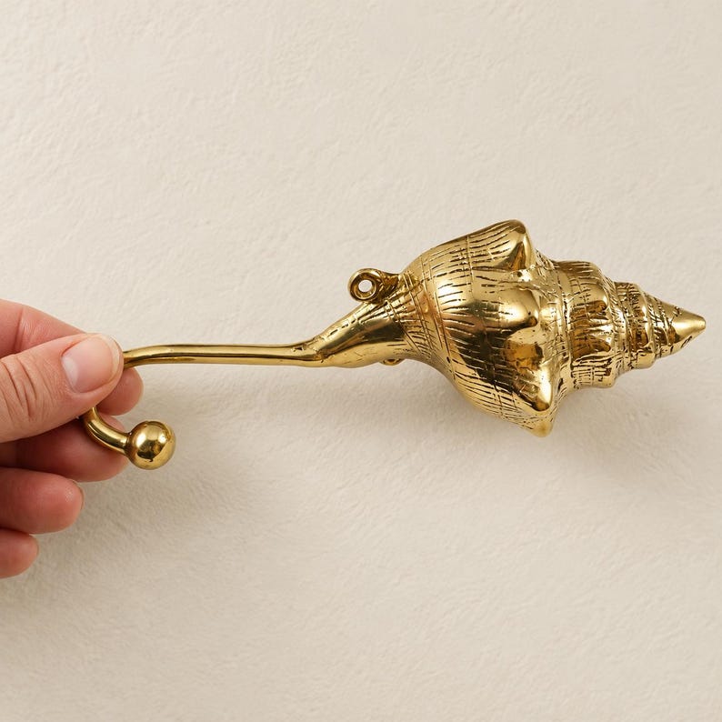 Hand holding a brass shell spiral hook, showing full length and curved hook end