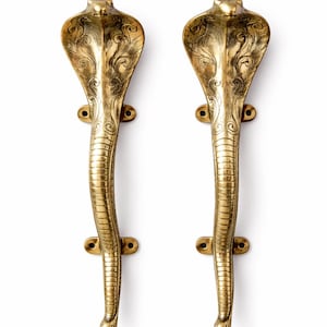 May include: A pair of brass cobra-shaped door handles. The gold-coloured handles feature detailed engraved patterns on the cobra's head and body. Each handle is mounted on a rectangular base with two screw holes.