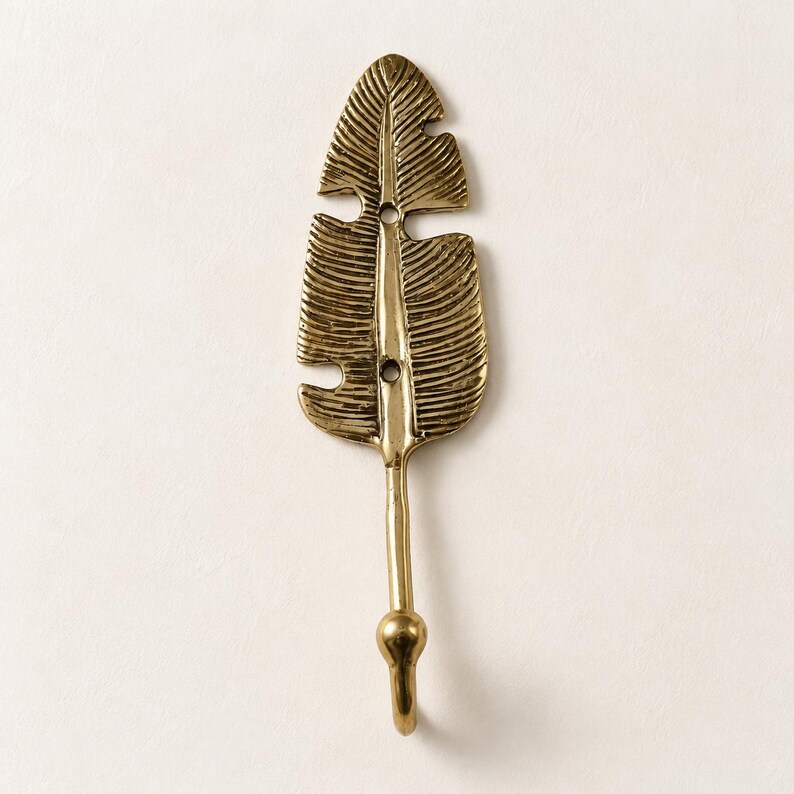 Single solid brass banana leaf hook mounted on a cream colored wall, close view of leaf shape and hook design