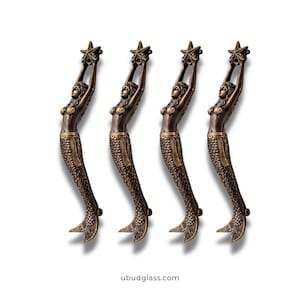 Könnte beinhalten: Vier bronzefarbene Türgriffe in Form von Meerjungfrauen. Jede Meerjungfrau hält einen Seestern über sich. Die Meerjungfrauen haben detaillierte Schuppen und sind in einer gebogenen Pose. Der Hintergrund ist weiß. Die Website ubudglass.com befindet sich unten.