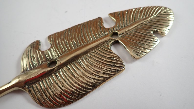 Macro close up of hand textured brass leaf hook surface showing detailed vein and leaf pattern engraving