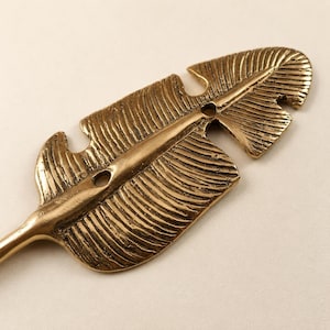 Close up detail of a solid brass banana leaf hook showing hand carved leaf vein texture