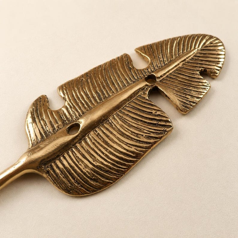 Close up detail of a solid brass banana leaf hook showing hand carved leaf vein texture