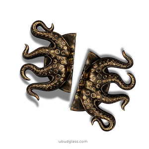 May include: Two bronze-colored octopus-shaped door handles. Each handle features a detailed design of an octopus tentacle with suction cups. The handles are mounted on a rectangular plate. The website address ubudglass.com is at the bottom.