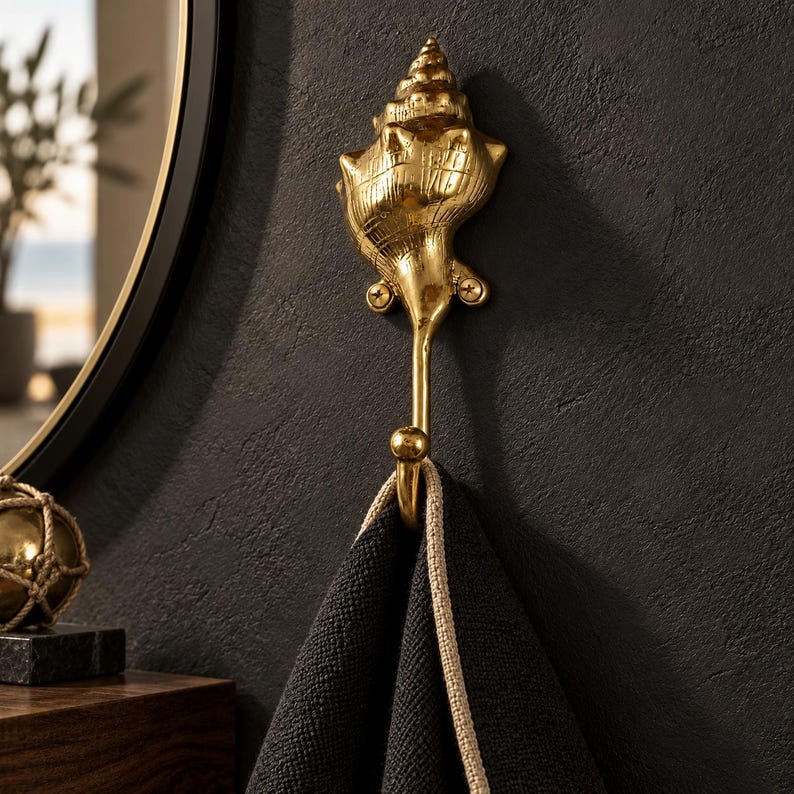 Brass shell spiral hook mounted on a dark wall near a round mirror, holding a black towel