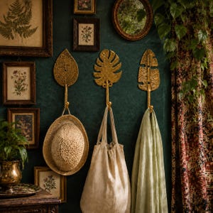 Brass leaf hooks styled in a dark green boho entryway with a woven hat, linen bag, and framed botanical art