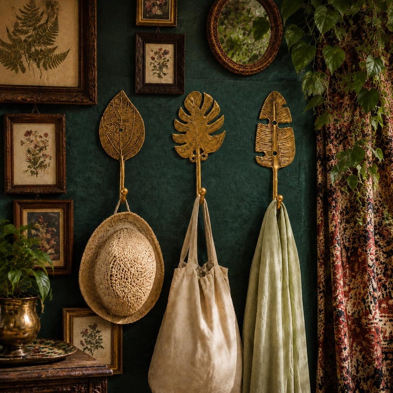 Brass leaf hooks styled in a dark green boho entryway with a woven hat, linen bag, and framed botanical art