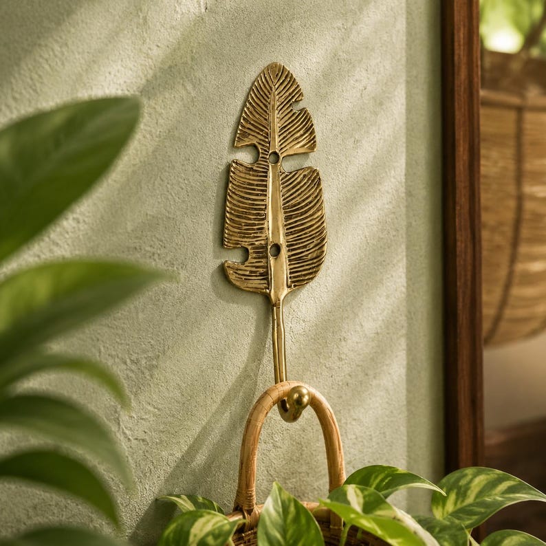 Solid brass banana leaf hook mounted on a textured wall surrounded by trailing green house plants, boho jungalow home decor