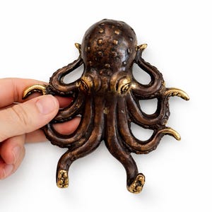 Hand holding solid brass octopus hook showing size and antique bronze finish
