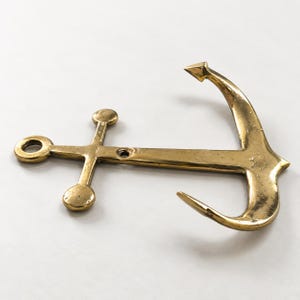 Brass anchor wall hook in an antique brass finish on a white background, angled view showing anchor shape and hook detail