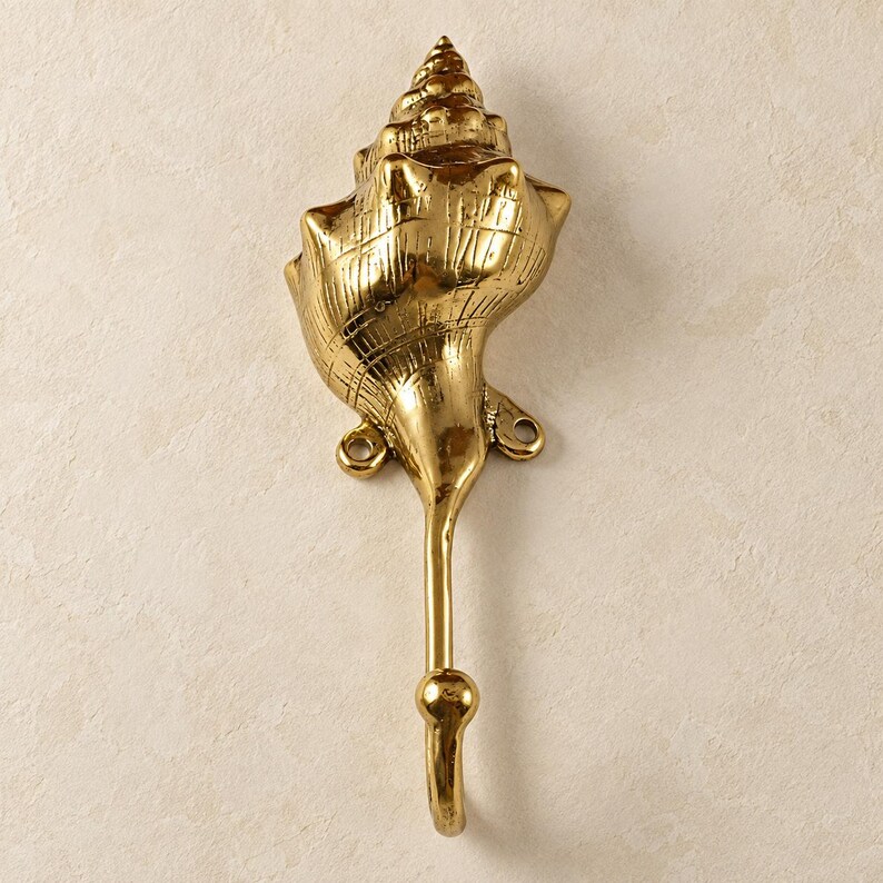 Brass shell spiral hook in a polished gold finish on a cream background