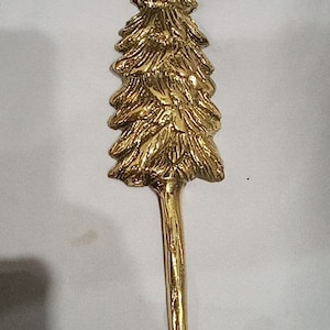 May include: A gold-toned metal hook shaped like a pine tree. The hook is designed to hang items on a wall.