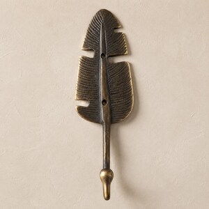 Brass leaf wall hook in a darker antique bronze finish mounted on a warm tan colored wall