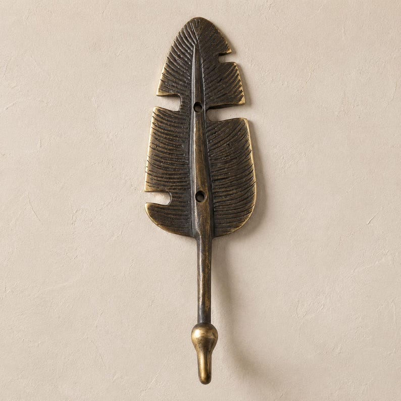 Brass leaf wall hook in a darker antique bronze finish mounted on a warm tan colored wall