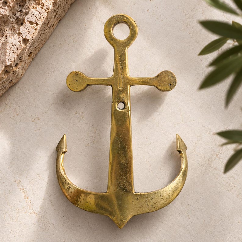Close up of brass anchor wall hook on a cream background showing anchor shape and hand cast brass texture, vintage nautical hardware