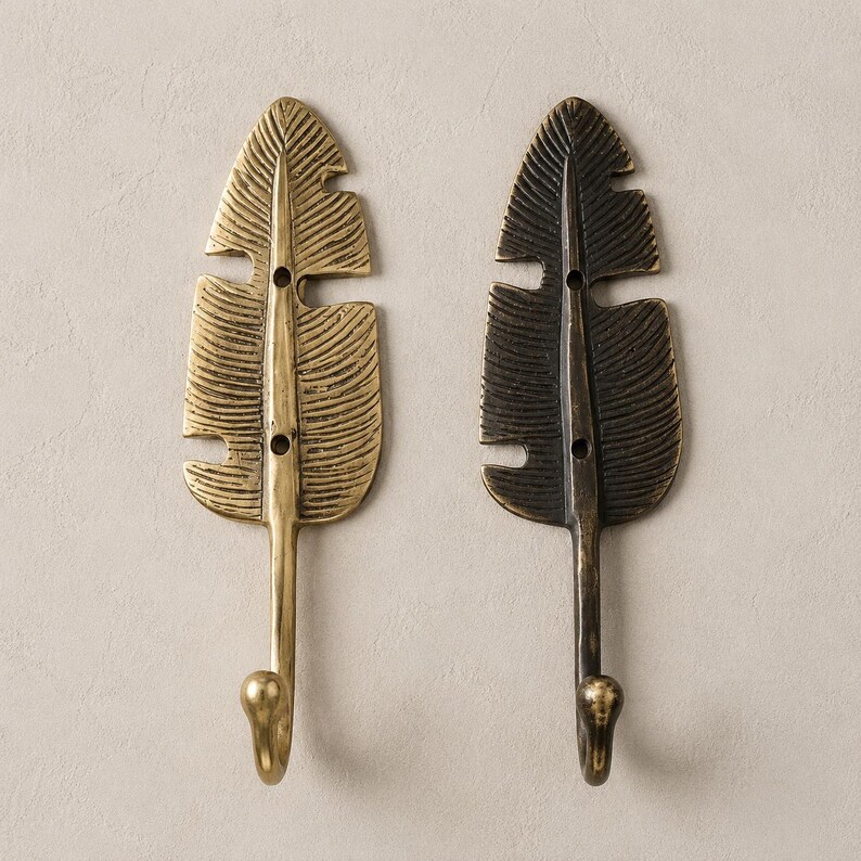 Two brass banana leaf hooks side by side showing antique bronze finish and polished brass finish options