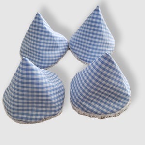 Peut inclure: Quatre articles en tissu vichy bleu et blanc, en forme de cône avec un bord frangé. Les articles sont disposés en carré sur fond blanc. Le tissu présente un motif à carreaux classique.