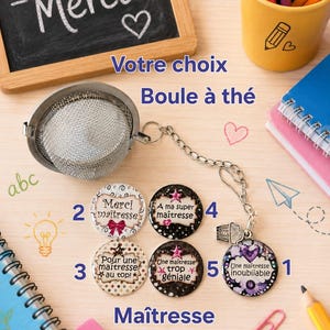 Puede incluir: Un infusor de té con cadena y dije, junto con botones decorativos con texto en francés. La imagen incluye una pequeña pizarra con "Merci" escrito, lápices y cuadernos. El tema es el agradecimiento a los profesores.