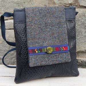 May include: A black faux leather crossbody bag with a tweed flap and a colorful button. The bag has a zipper closure and a long strap.